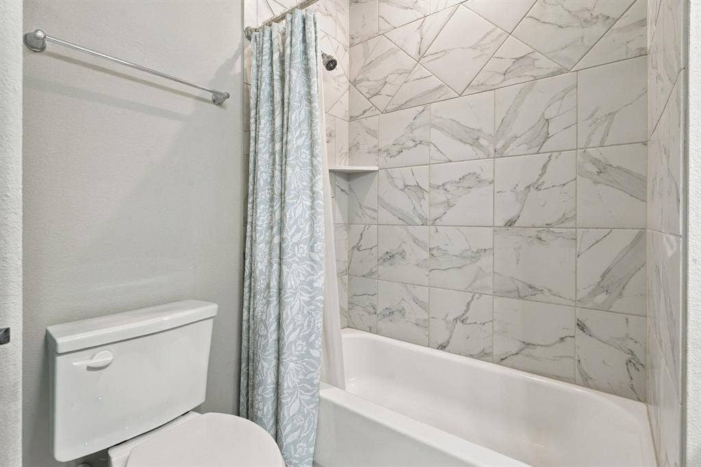 Full-height shower enclosure featuring stone-patterned square tile, a built-in recessed soap niche, a white porcelain bathtub, and a chrome towel bar