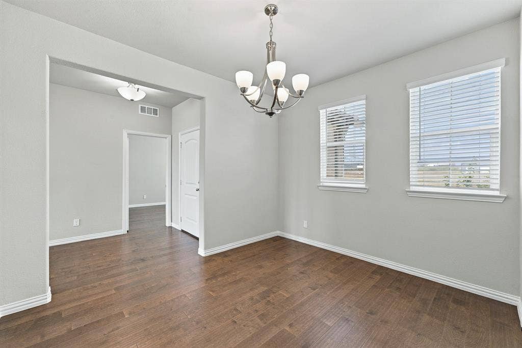 Wood-finish flooring, neutral wall tones, multi-light brushed-nickel chandelier, and dual windows with horizontal blinds