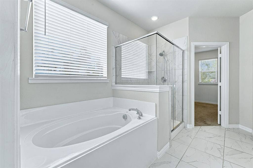 Soaking tub with a deck-mounted faucet, walk-in shower with a glass enclosure and wall-mounted showerhead, and large-format tile flooring