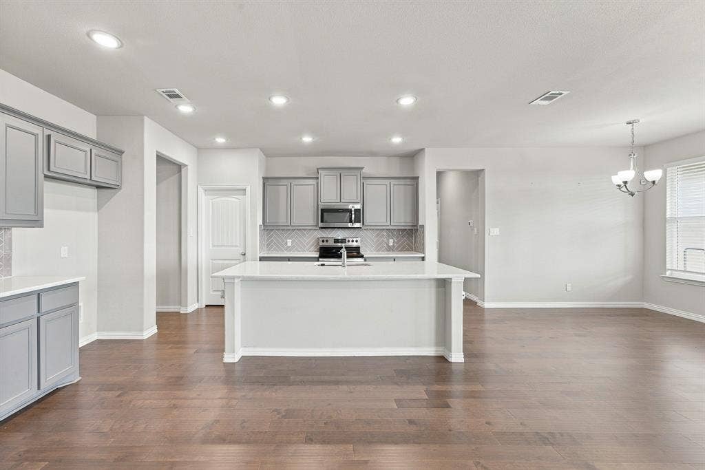 Kitchen featuring a central island with white countertops, grey shaker-style cabinetry, stainless steel appliances, herringbone-pattern tile backsplash, and wood-finish flooring