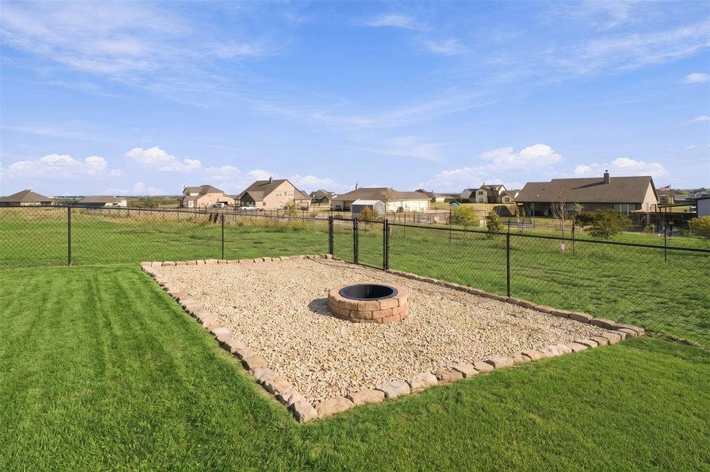 Backyard featuring a gravel-surrounded fire pit with stone masonry trim and a black chain-link perimeter fence