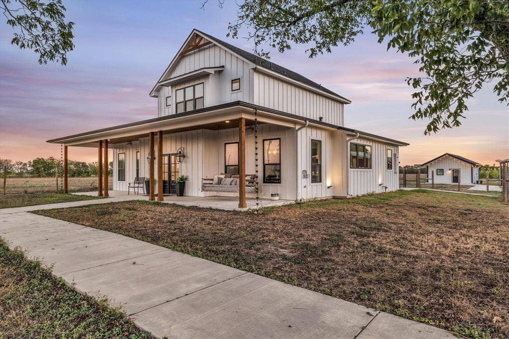 23010 Rosebud Road, Burlington, TX 76519 Board-and-batten siding, covered wrap-around porch, natural timber structural posts, metal chain-style downspouts, and detached auxiliary structure