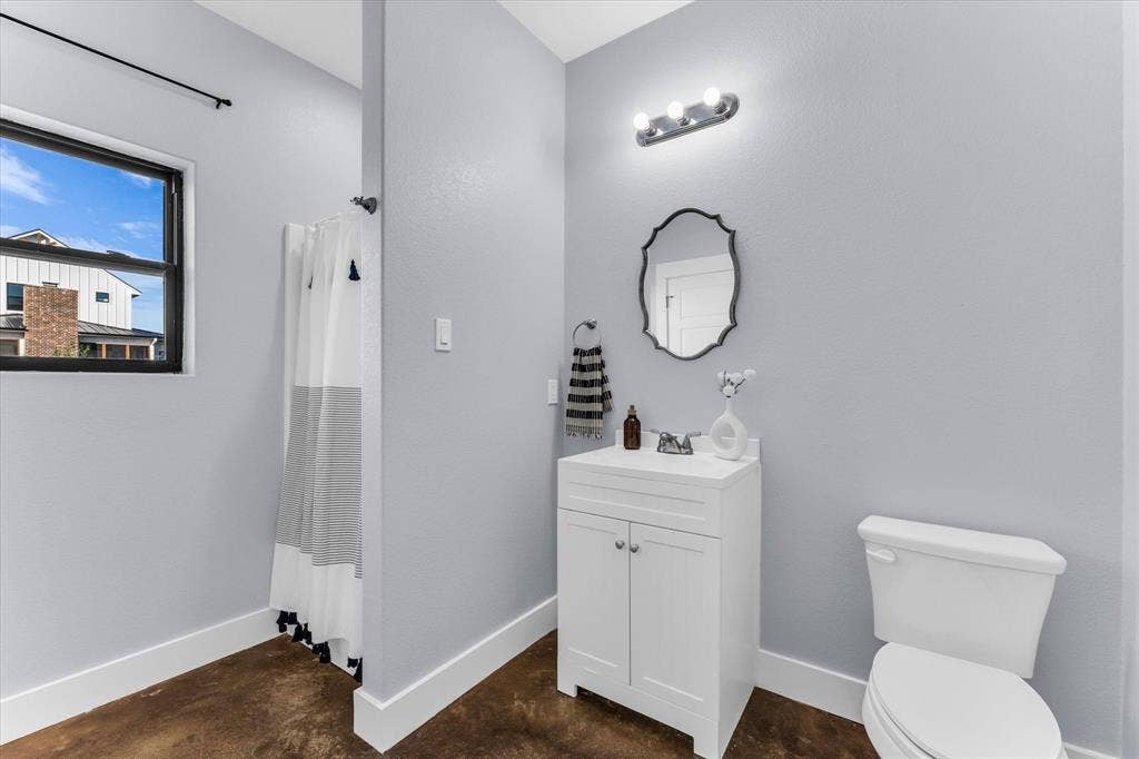 23010 Rosebud Road, Burlington, TX 76519 White vanity cabinet with integrated basin, polished metal faucet, scalloped wall mirror, three-light vanity fixture, and stained concrete flooring