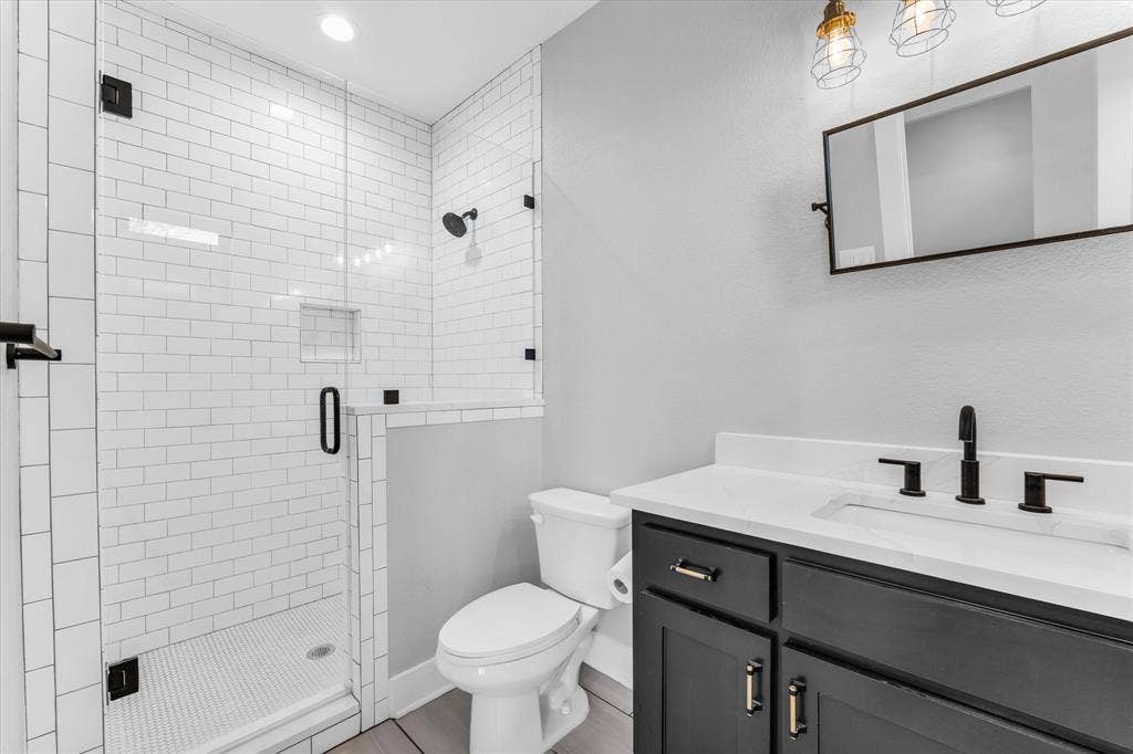 23010 Rosebud Road, Burlington, TX 76519 Bathroom featuring a walk-in shower with white subway tile, a glass enclosure, a vanity with a white countertop, matte black fixtures, and a framed mirror
