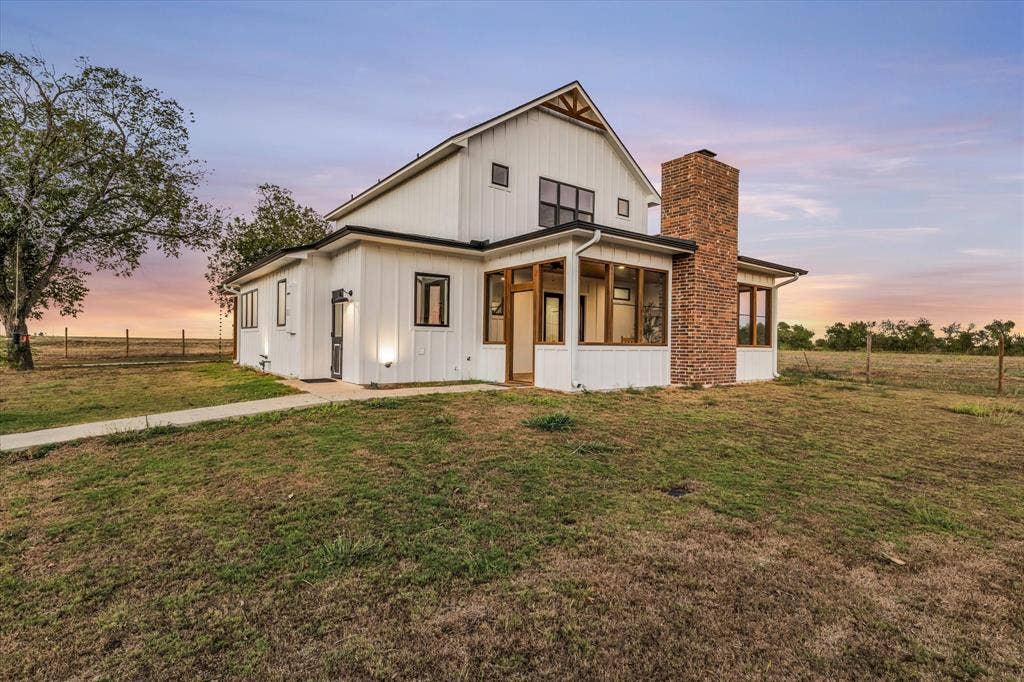 23010 Rosebud Road, Burlington, TX 76519 Modern farmhouse exterior featuring vertical white siding, a prominent brick chimney, and a covered porch with timber-framed accents