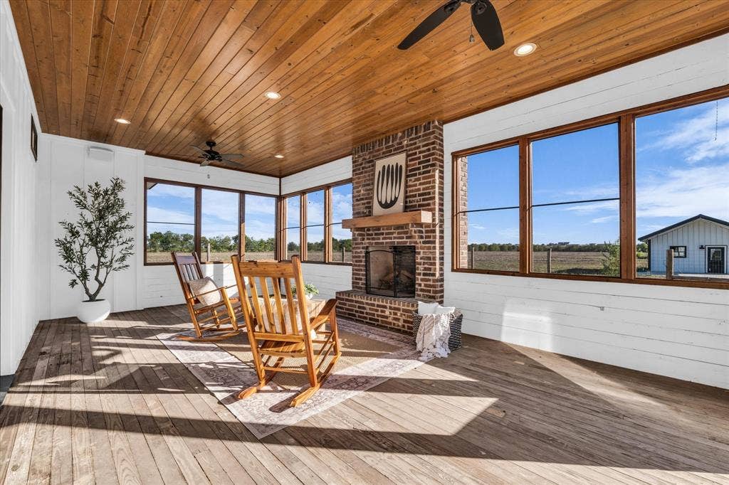 23010 Rosebud Road, Burlington, TX 76519 Enclosed porch featuring wood-plank ceiling, exposed brick fireplace with timber mantel, expansive windows, recessed lighting, and wood-finish flooring