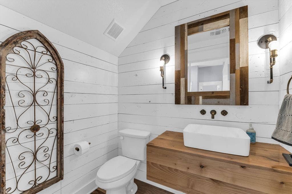 23010 Rosebud Road, Burlington, TX 76519 Bathroom featuring white horizontal shiplap wall paneling, a wood-finish floating vanity with a rectangular vessel sink, and dual wall-mounted light fixtures