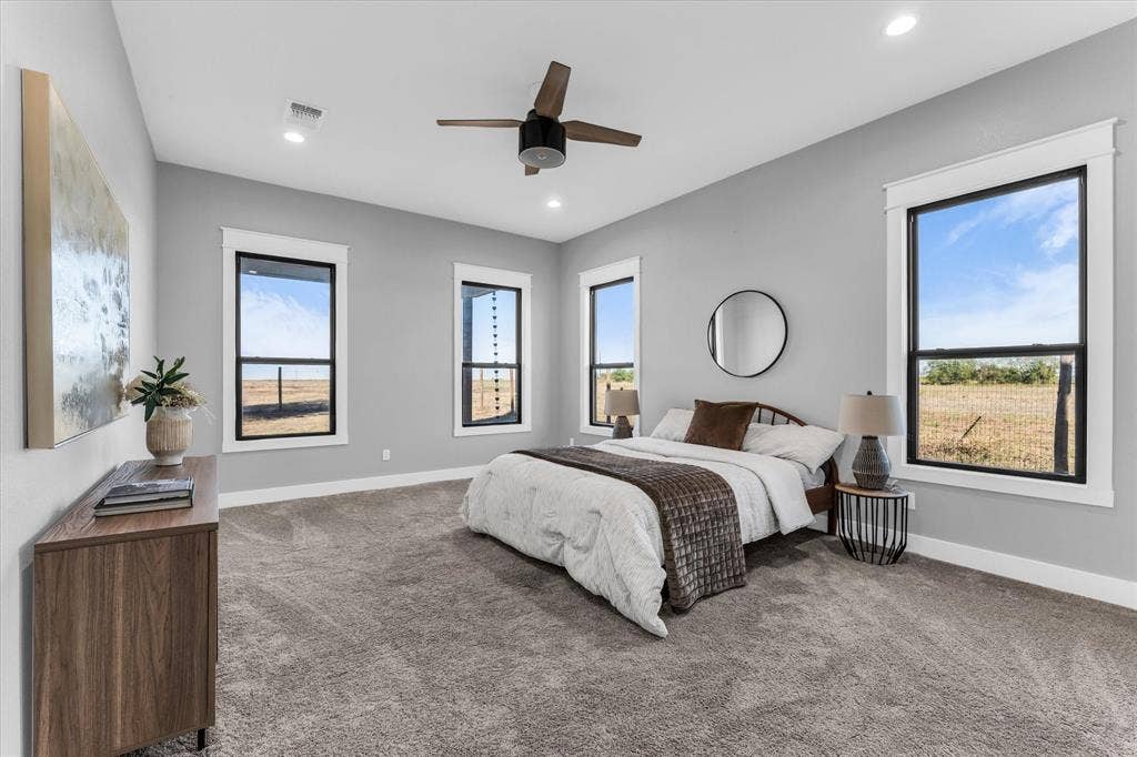 23010 Rosebud Road, Burlington, TX 76519 Neutral-toned interior featuring expansive windows with black frames, carpeted flooring, recessed lighting, and a centrally mounted ceiling fan
