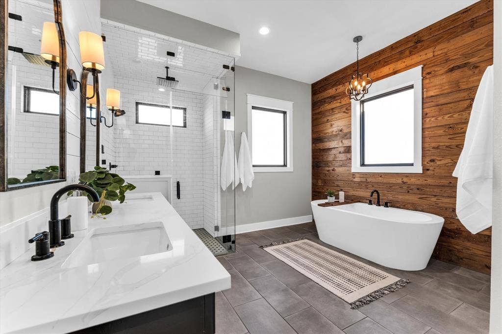 23010 Rosebud Road, Burlington, TX 76519 Bathroom featuring a double vanity with quartz countertops, a walk-in glass-enclosed shower with subway tile surround, a freestanding soaking tub, wood-plank accent wall, and tile flooring