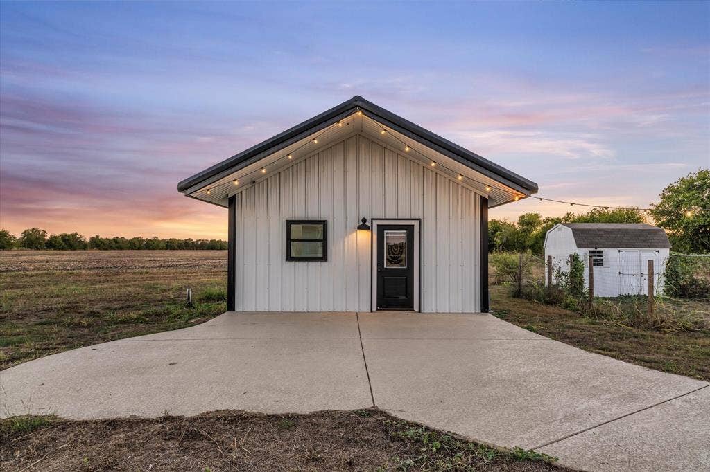 23010 Rosebud Road, Burlington, TX 76519 Exterior featuring white vertical metal siding, dark trim, concrete driveway, and attached outdoor lighting