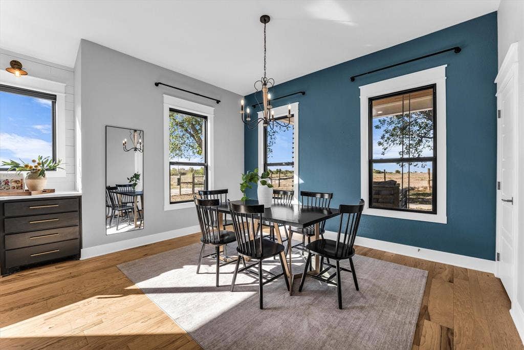 23010 Rosebud Road, Burlington, TX 76519 Wood-finish flooring, accent wall, multi-pane windows with black frames, built-in cabinetry with hardware, and hanging chandelier