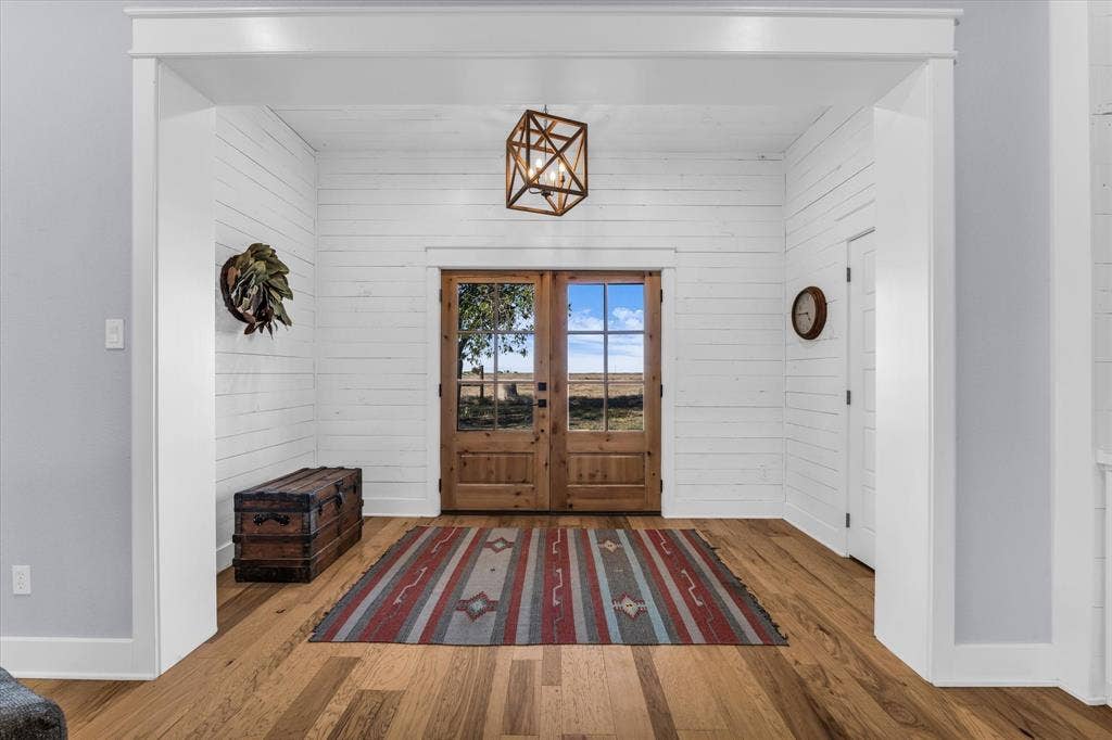 23010 Rosebud Road, Burlington, TX 76519 Entryway featuring white horizontal shiplap wall paneling, wood-finish flooring, a geometric pendant light fixture, and double entry doors with glass panes