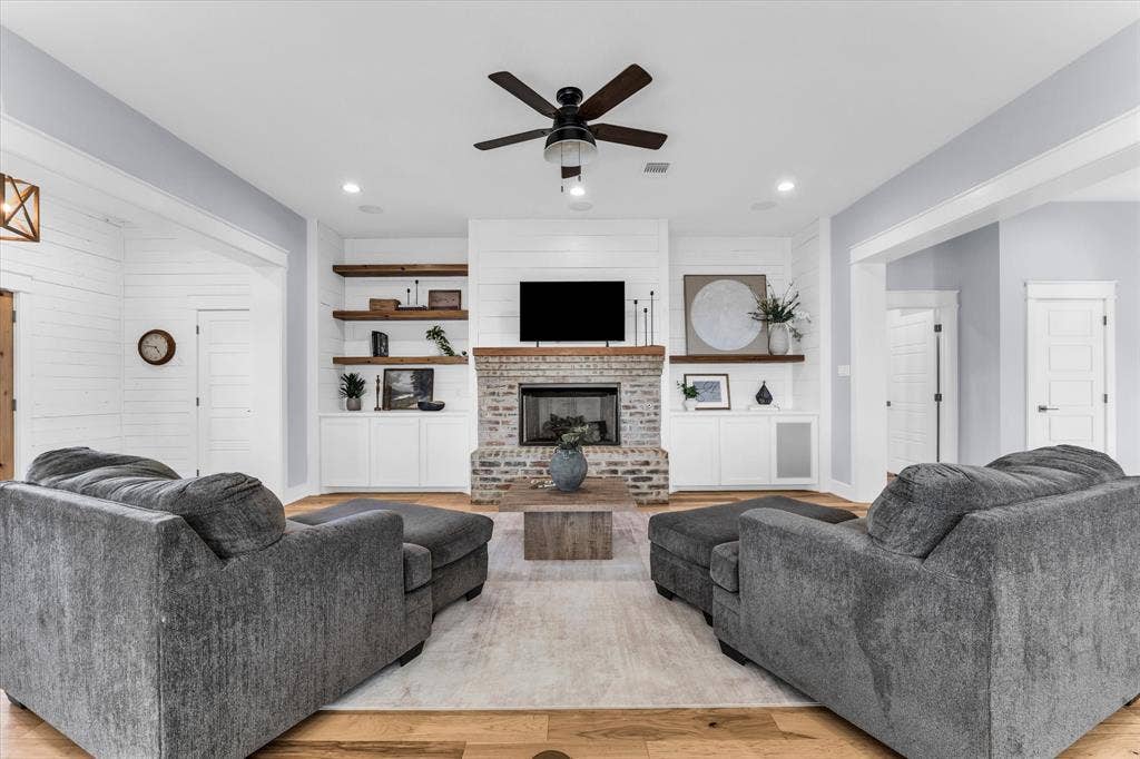 23010 Rosebud Road, Burlington, TX 76519 Brick fireplace featuring a wood mantel, floor-to-ceiling shiplap detailing, built-in lower cabinetry, and floating wood shelving