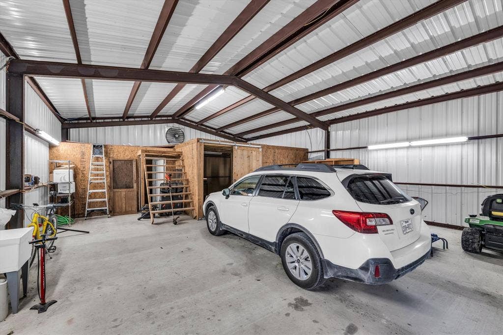 23010 Rosebud Road, Burlington, TX 76519 Expansive workshop featuring exposed steel beam construction, corrugated metal walls and ceiling, high-clearance open-span design, concrete flooring, and built-in wooden structure with integrated staircase