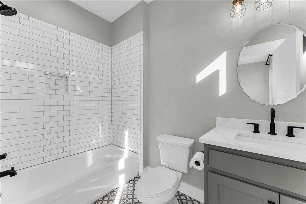23010 Rosebud Road, Burlington, TX 76519 Bathroom featuring a tub-shower combination with white subway tile surround, recessed wall niche, vanity with stone-finish countertop, matte black fixtures, and patterned tile flooring