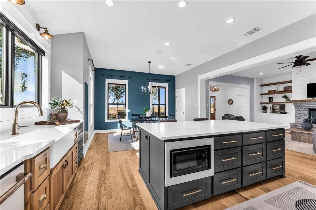 23010 Rosebud Road, Burlington, TX 76519 Kitchen featuring a large central island with dark cabinetry, stone-finish countertops, apron-front farmhouse sink with bronze-tone faucet, and wood-finish flooring