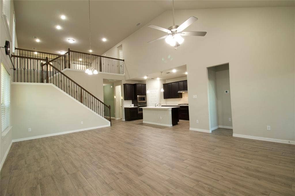 Vaulted ceilings, wood-finish flooring, staircase with metal balusters, recessed lighting, and kitchen featuring dark cabinetry and a central island