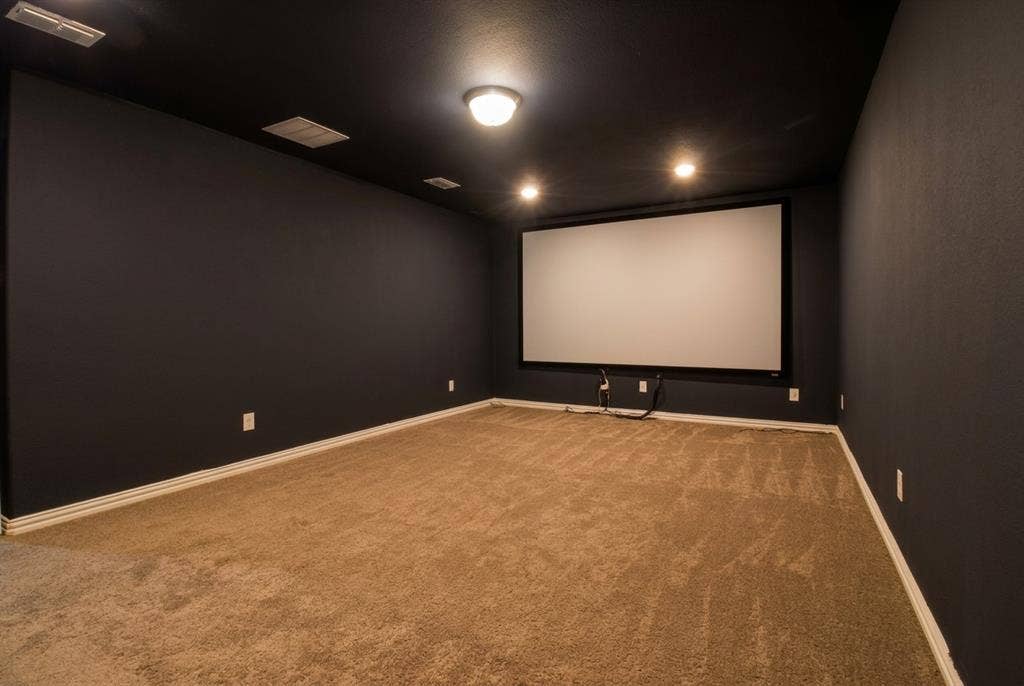 Dedicated media space featuring dark-toned walls and ceiling, wall-mounted projection screen, and carpeting