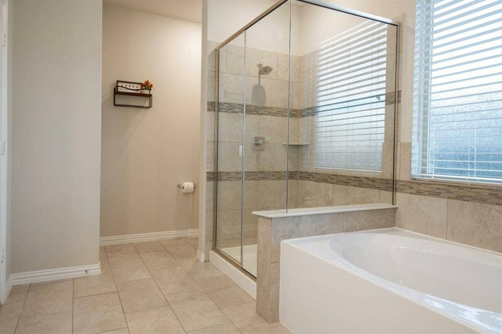 Walk-in shower with a glass enclosure, tile surround featuring decorative mosaic inlay, built-in soaking tub, and tile flooring