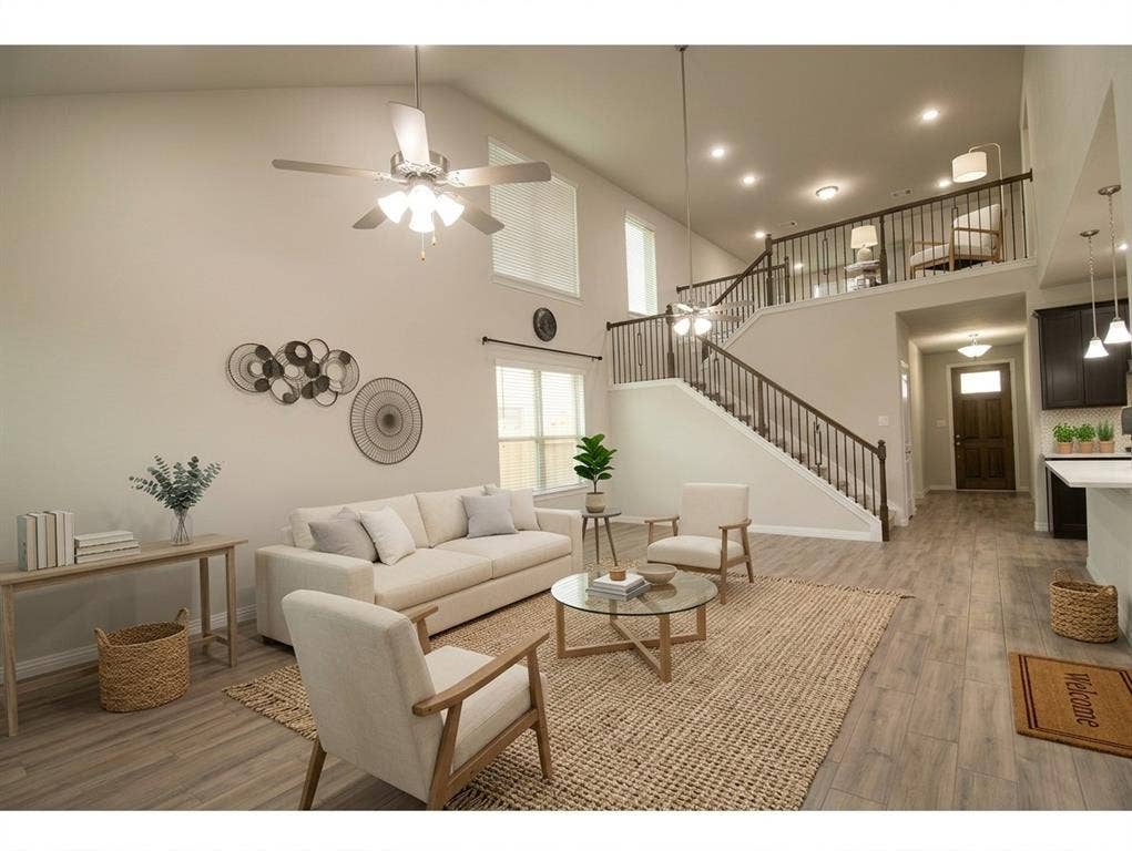 High-ceiling living area featuring wood-finish flooring, recessed lighting, ceiling fan with light kit, and open staircase with metal balusters