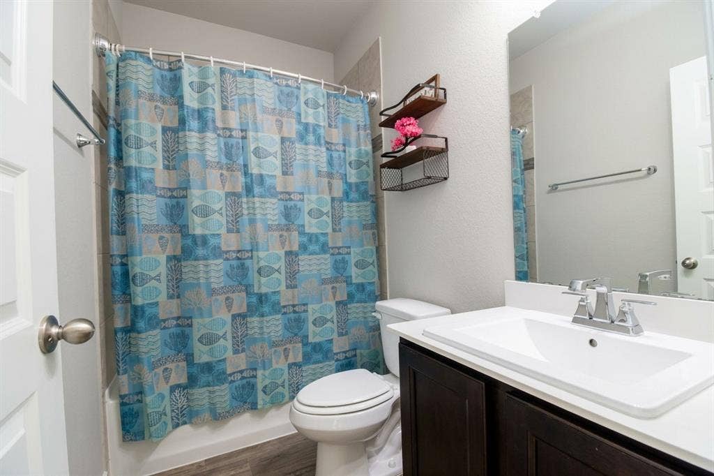 Bathroom featuring a vanity with a white integrated sink, dark wood-finish cabinetry, a full-width wall mirror, and a shower-tub combination with tile surround