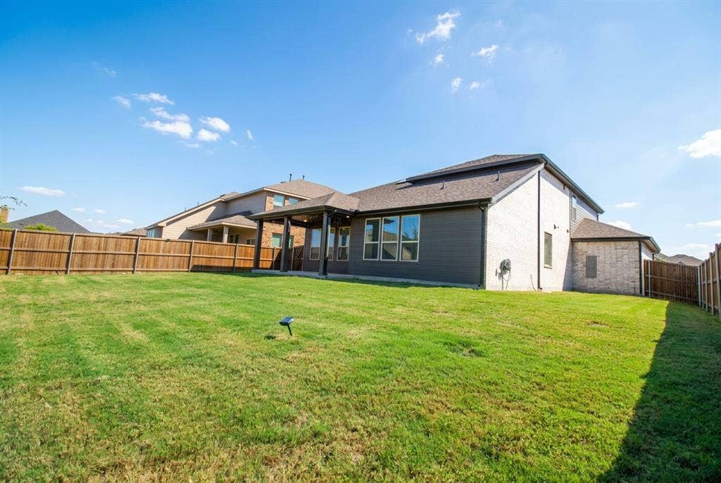 Rear exterior featuring a covered patio, brick and horizontal siding facade, asphalt shingle roof, and a fenced backyard