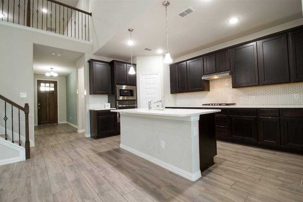Kitchen featuring dark wood cabinetry, an island with a light-toned countertop, wood-finish flooring, a hexagonal tile backsplash, and recessed lighting
