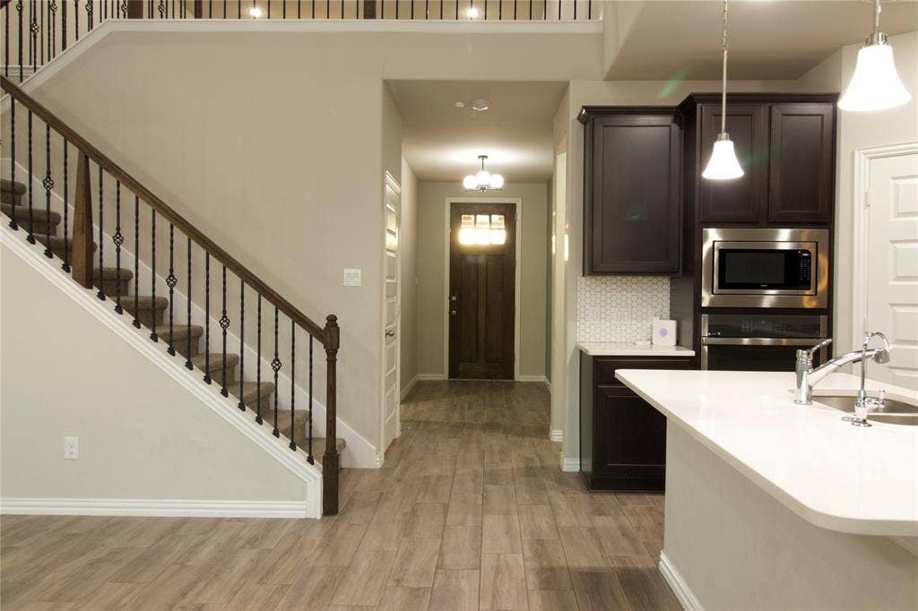 Entry featuring wood-finish flooring, staircase with decorative metal balusters, dark wood-tone cabinetry, quartz countertops, and a built-in double oven