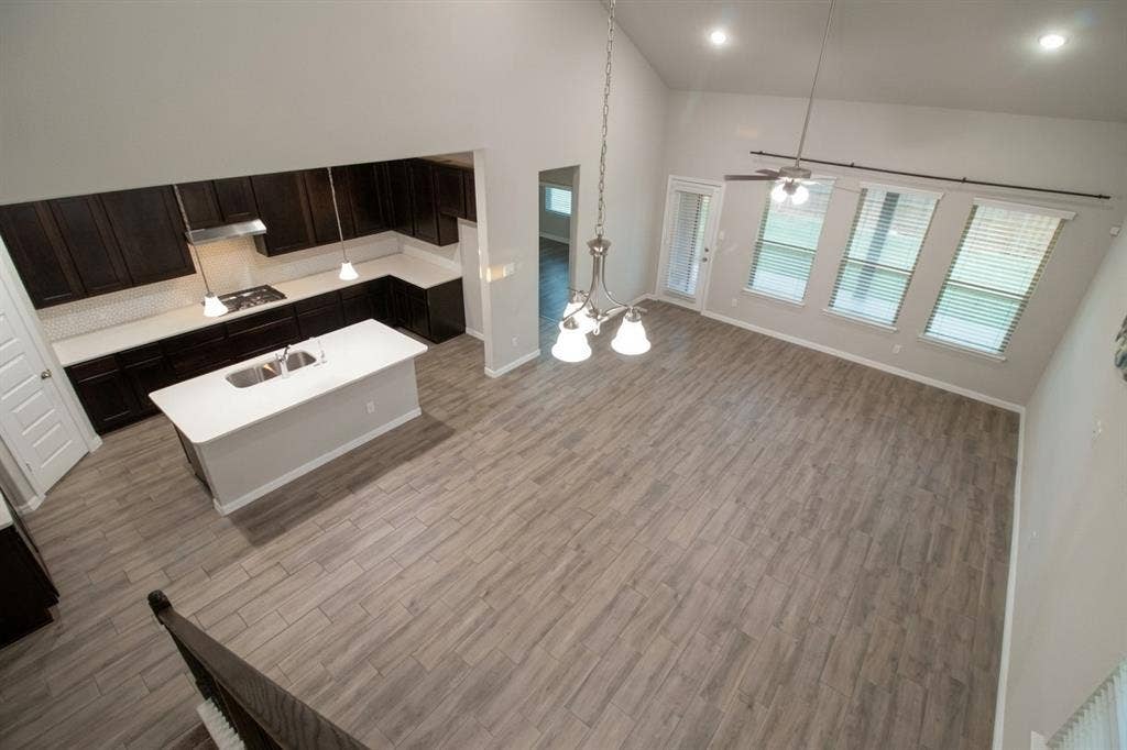 Open-concept interior featuring vaulted ceilings, wood-finish flooring, dark-toned cabinetry, a kitchen island with a neutral countertop, and large windows