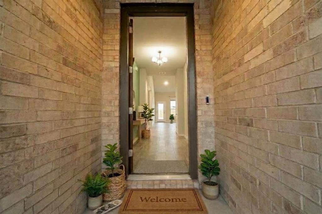 Entryway featuring textured brick masonry walls, a tall neutral-toned door, and tile flooring