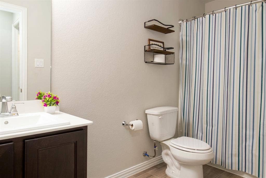 Bathroom featuring a vanity with dark-finish cabinetry, a white countertop with an integrated basin, a polished chrome faucet, and wood-finish flooring