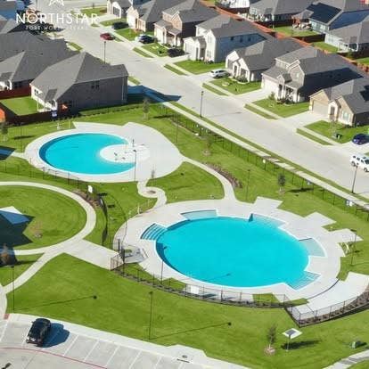 Community recreation area featuring two circular swimming pools, concrete sun decks, landscaped lawn areas, and paved walkways