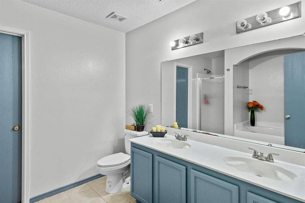 600 Claiborn Lane, Wylie, TX 75098 Dual-basin vanity with solid-surface countertop, full-width wall mirror, brushed metal multi-light fixtures, and tiled flooring