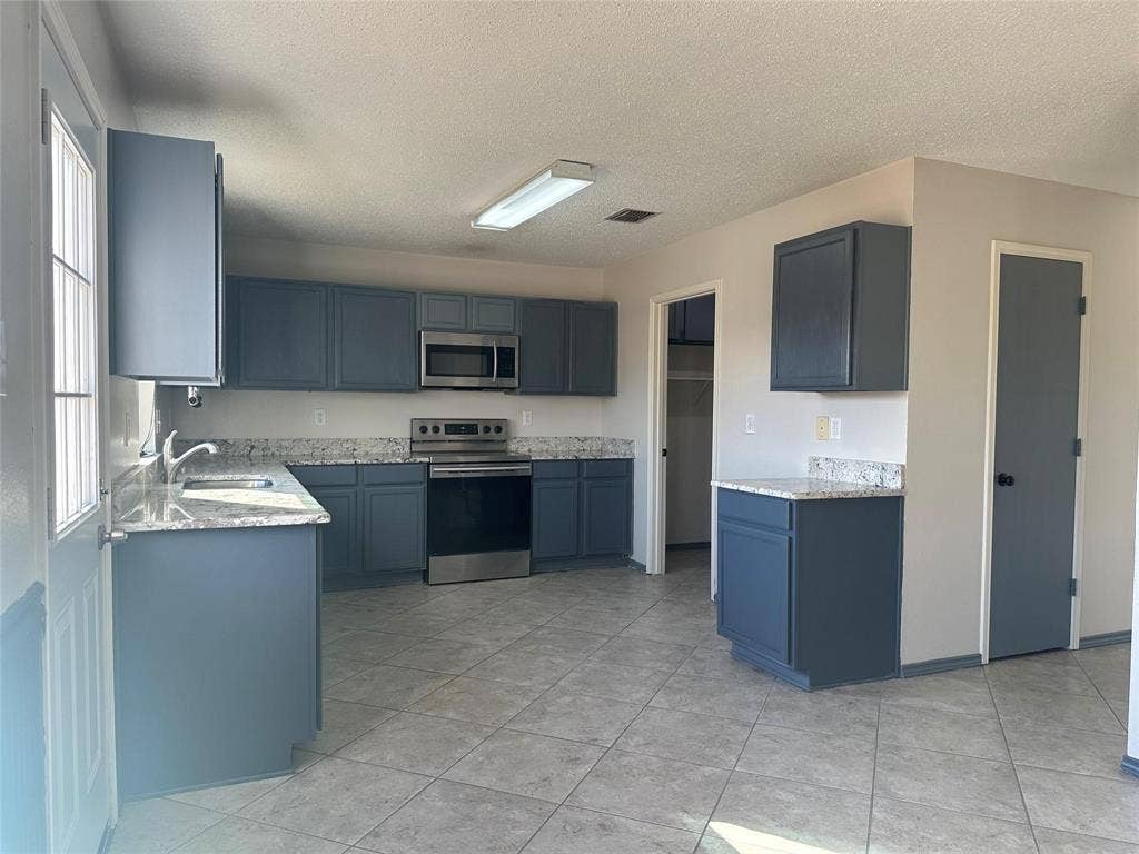 600 Claiborn Lane, Wylie, TX 75098 Kitchen featuring slate-blue cabinetry, stone-finish countertops, stainless steel appliances, and diagonal tile flooring