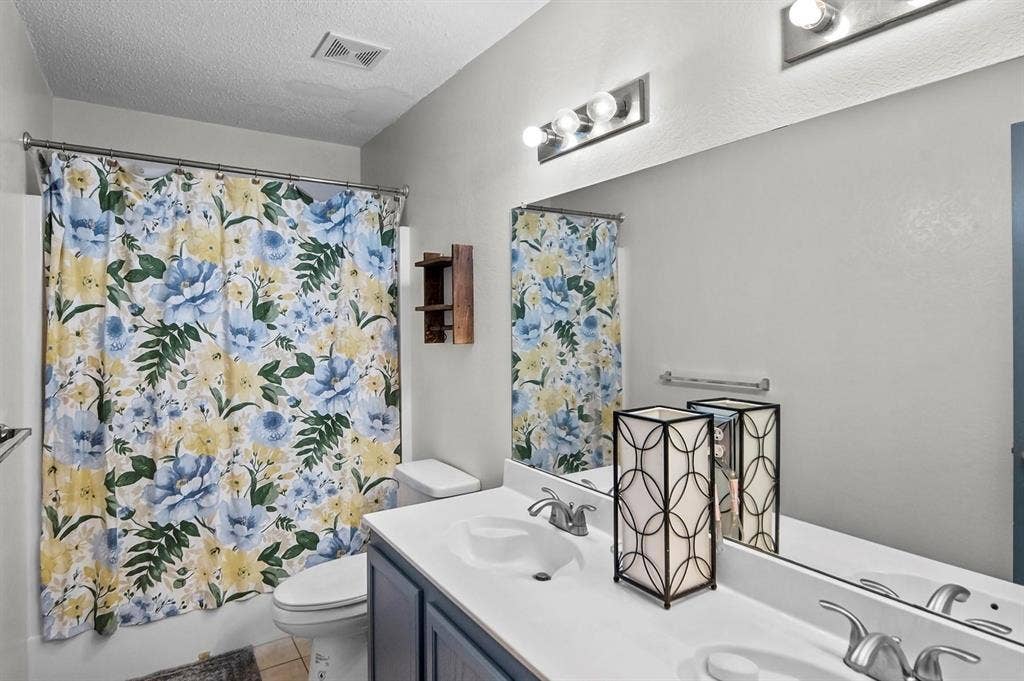 600 Claiborn Lane, Wylie, TX 75098 Bathroom featuring a dual-sink vanity with a solid-surface countertop, full-width wall mirror, chrome fixtures, and a shower-tub combination