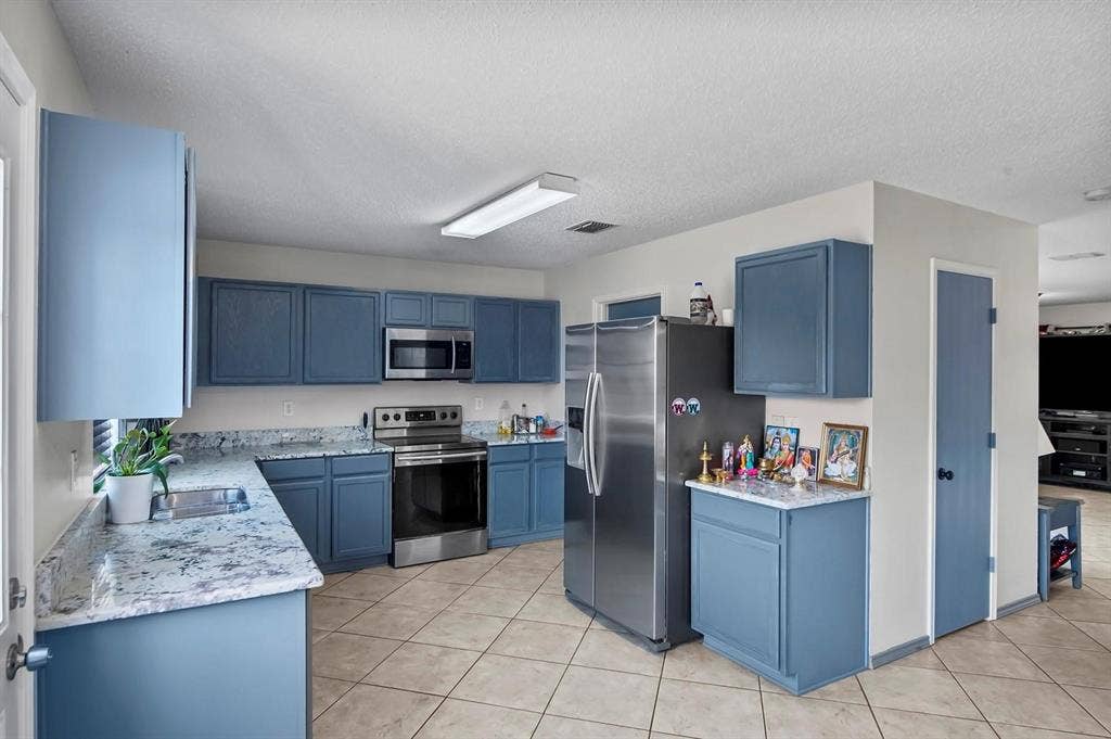600 Claiborn Lane, Wylie, TX 75098 Kitchen featuring blue cabinetry, stone-finish countertops, stainless steel appliances, and tile flooring