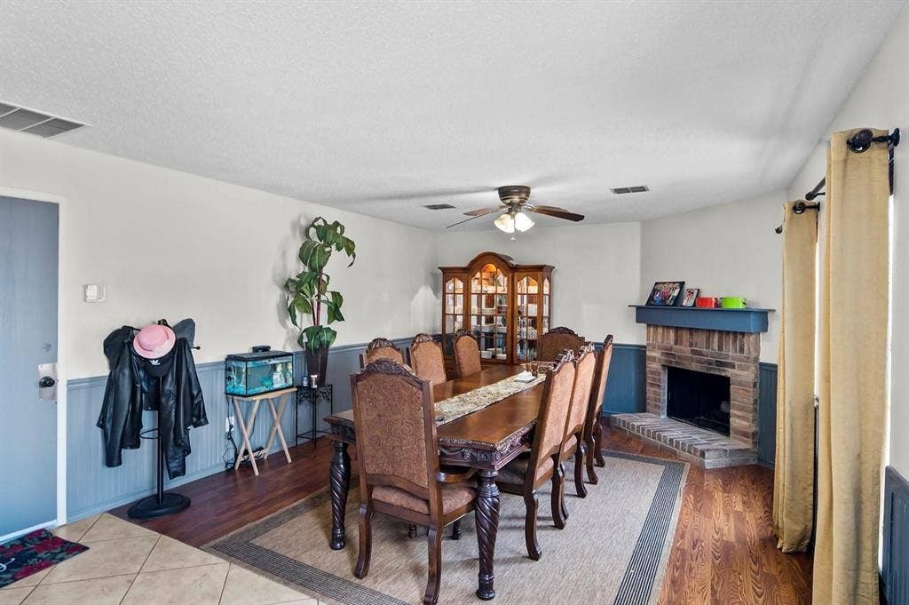 600 Claiborn Lane, Wylie, TX 75098 Dining area featuring wood-finish flooring, two-toned wall paneling, a masonry corner fireplace with a mantel, and a ceiling fan with integrated lighting