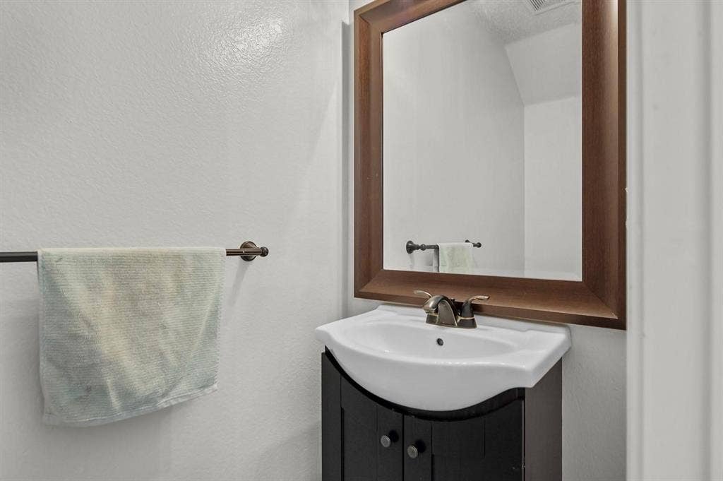 600 Claiborn Lane, Wylie, TX 75098 Curved dark wood vanity featuring a white ceramic sink, metallic faucet, and a coordinating dark wood-framed mirror