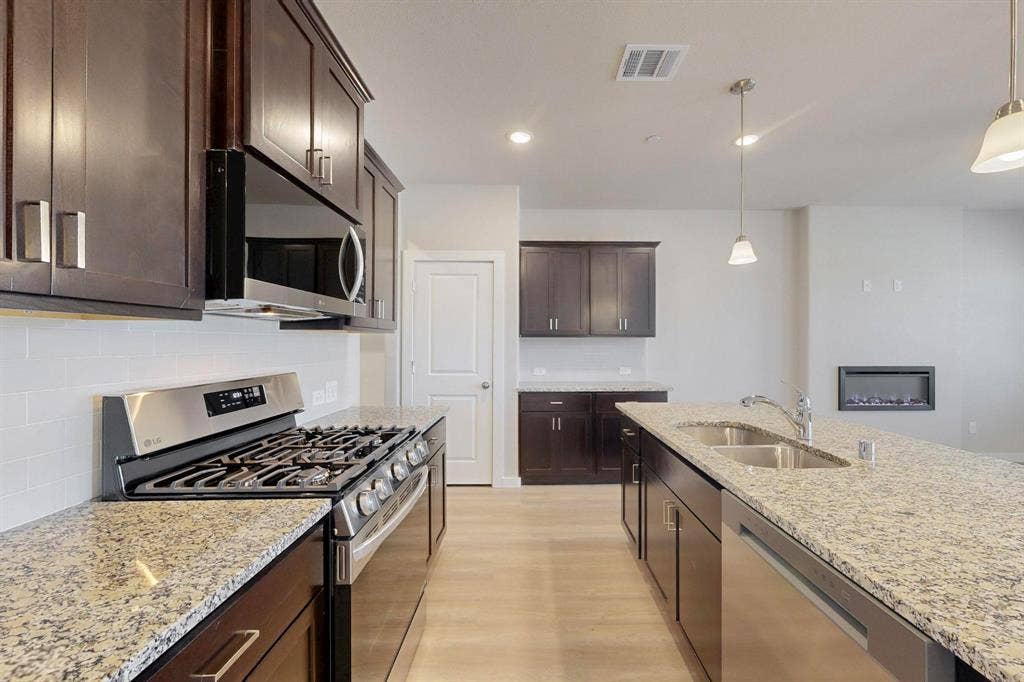 1428 Starlight Trail, Mesquite, TX 75181 Kitchen featuring appliances with stainless steel finishes, light stone countertops, dark brown cabinets, recessed lighting, and a glass covered fireplace