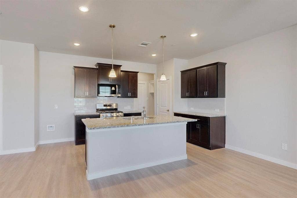 1428 Starlight Trail, Mesquite, TX 75181 Kitchen with dark brown cabinets, stainless steel appliances, light wood-style floors, light stone countertops, and a kitchen island with sink