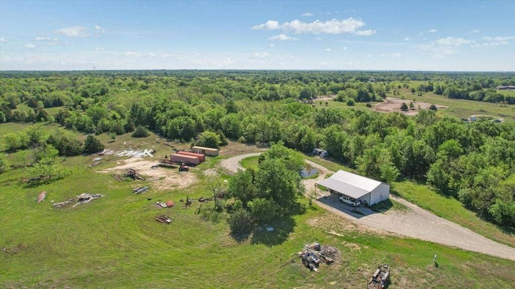 2377 FM 36 N, Farmersville, TX 75442 Expansive acreage featuring a metal-roofed structure, gravel driveway, mature trees, and a pond