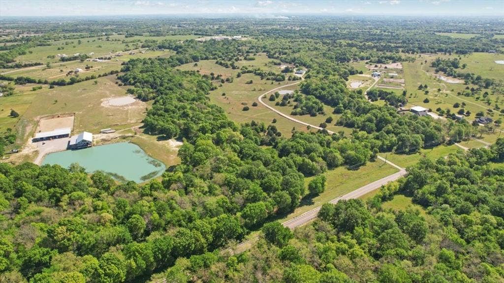 2377 FM 36 N, Farmersville, TX 75442 Expansive acreage featuring a private pond, metal-roofed outbuildings, mature tree clusters, and paved road access