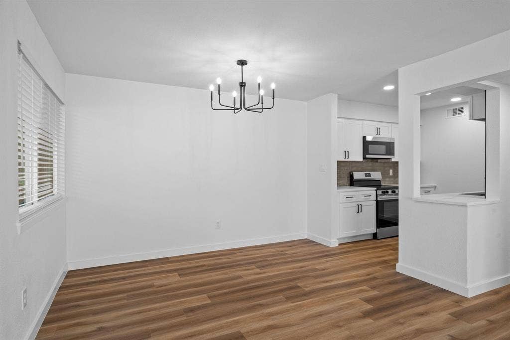 2621 Amherst Court, Irving, TX 75038 Open-concept space featuring wood-finish flooring, a modern multi-arm chandelier, white cabinetry, and a pass-through counter