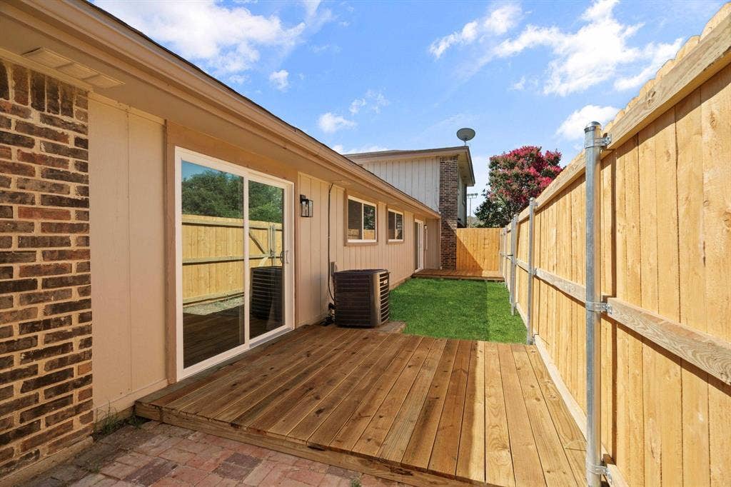 2621 Amherst Court, Irving, TX 75038 Rear exterior featuring a wood deck, brick and siding facade, sliding glass door, and wood privacy fencing