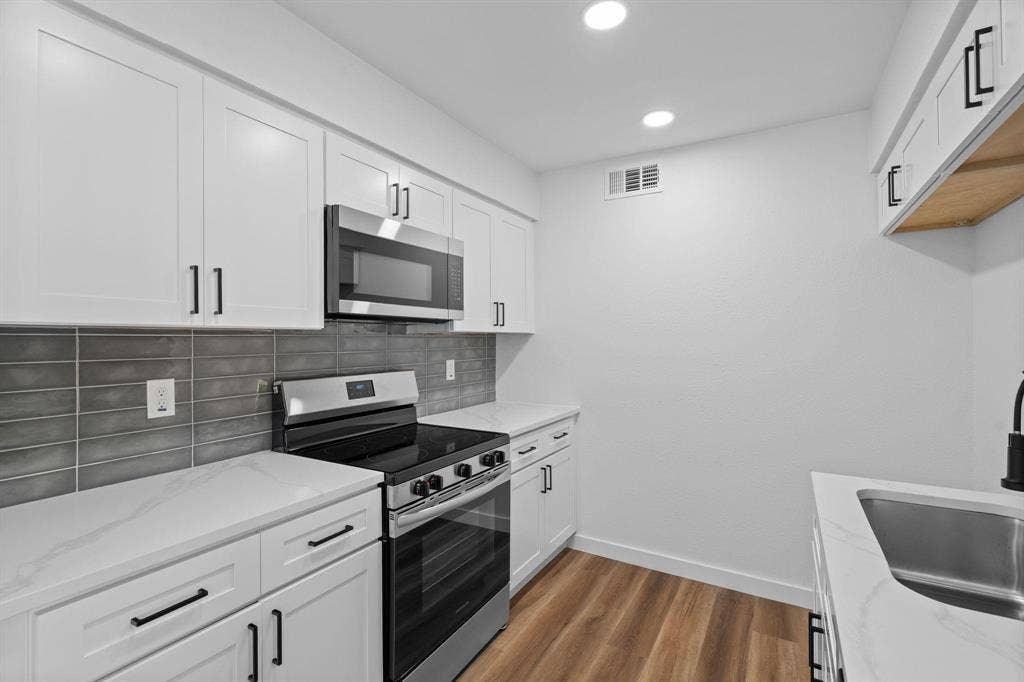 2621 Amherst Court, Irving, TX 75038 Kitchen featuring white shaker-style cabinetry, quartz countertops, gray subway tile backsplash, stainless steel appliances, and wood-finish flooring