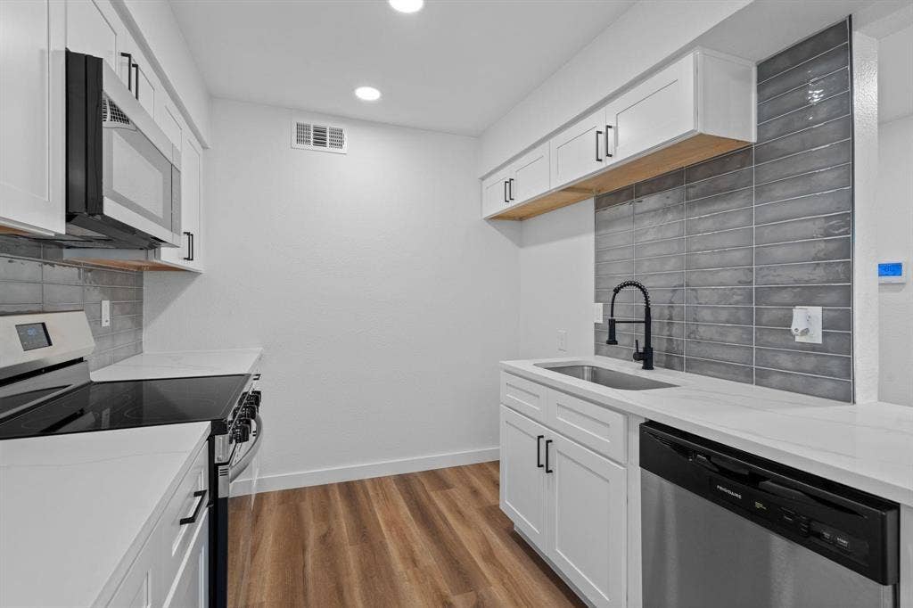 2621 Amherst Court, Irving, TX 75038 Kitchen featuring white shaker-style cabinetry, white countertops, gray elongated tile backsplash, stainless steel appliances, and wood-finish flooring