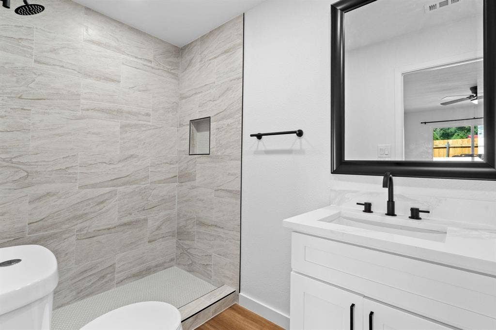 2621 Amherst Court, Irving, TX 75038 Bathroom featuring a vanity with a stone-surface countertop, matte black widespread faucet, framed mirror, and walk-in shower with stone-style wall tile and a built-in recessed niche