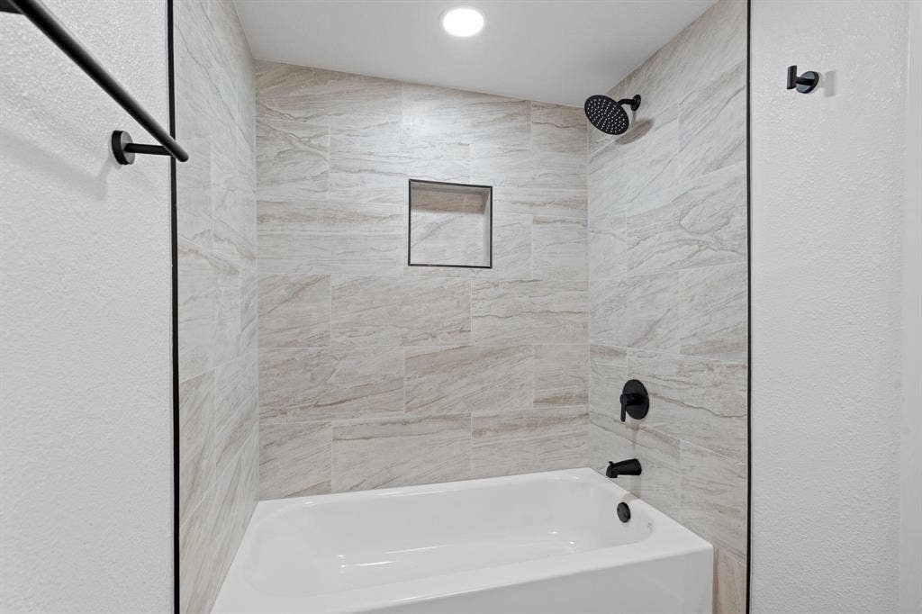 2621 Amherst Court, Irving, TX 75038 Bathtub surround featuring large-format neutral-toned tile, recessed wall niche, matte black fixtures, and a shower head