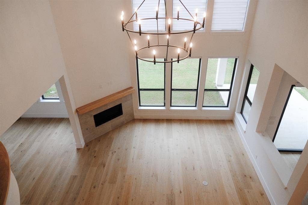 10694 Hollydale Lane, Frisco, TX 75035 Double-height living area featuring wood-finish flooring, a contemporary iron chandelier, a floor-to-ceiling window arrangement, and a fireplace with a light-tone tile surround and wood mantel