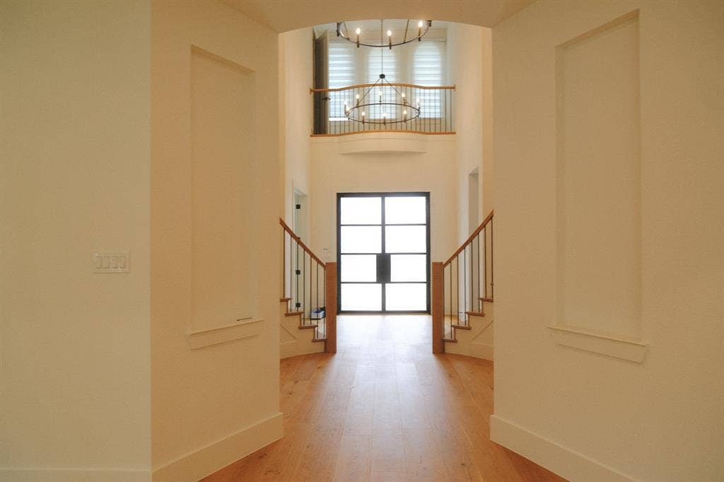 10694 Hollydale Lane, Frisco, TX 75035 Foyer featuring wood-finish flooring, two recessed wall niches, dual-staircase architecture with wooden handrails, and a multi-panel grid-style door